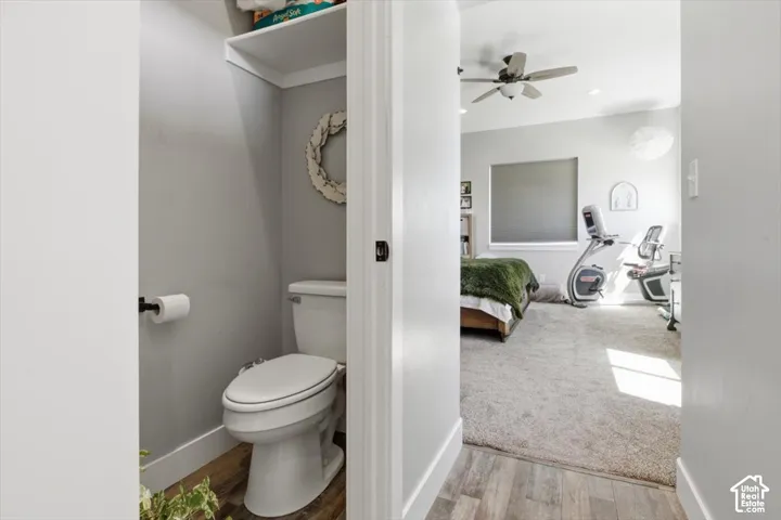 Enclosed water closet featuring wood-finish flooring, a white toilet, and a built-in overhead storage shelf