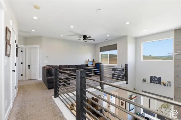 Interior landing featuring dark-stained wood railing with horizontal metal balusters, recessed lighting, neutral carpeting, and a wood-panel accent wall