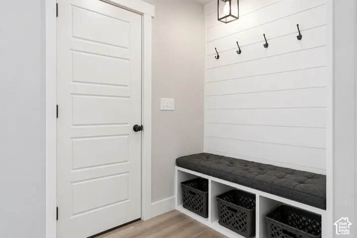Built-in mudroom bench featuring three open storage compartments, white shiplap wall paneling, matte black wall-mounted hooks, and a geometric cage-style light fixture