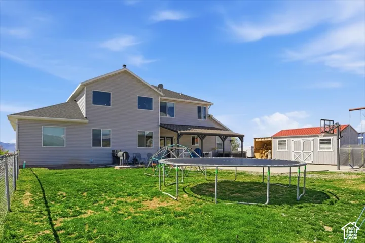 Rear exterior featuring light-colored horizontal siding, a covered patio with metal roofing, a detached storage building with a metal roof, and chain-link perimeter fencing