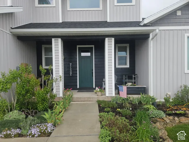 Covered front porch featuring board-and-batten siding, square columns, a dark-toned accent wall, and a concrete walkway bordered by tiered garden beds