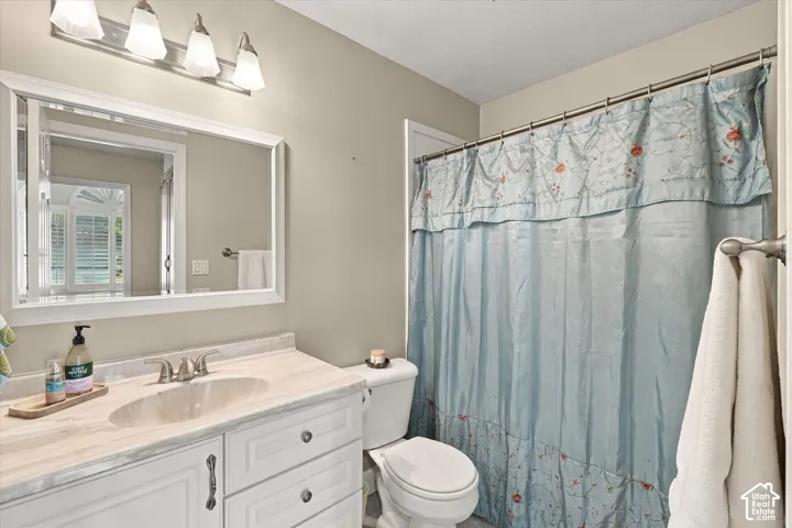 Bathroom vanity featuring white cabinetry, a neutral-toned stone-finish countertop with an integrated oval sink, a wall-mounted four-light fixture, and a white-framed mirror