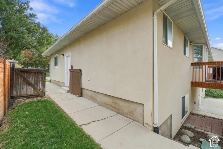 Stucco exterior featuring an elevated wood-railing deck, concrete walkway, and wood privacy fencing