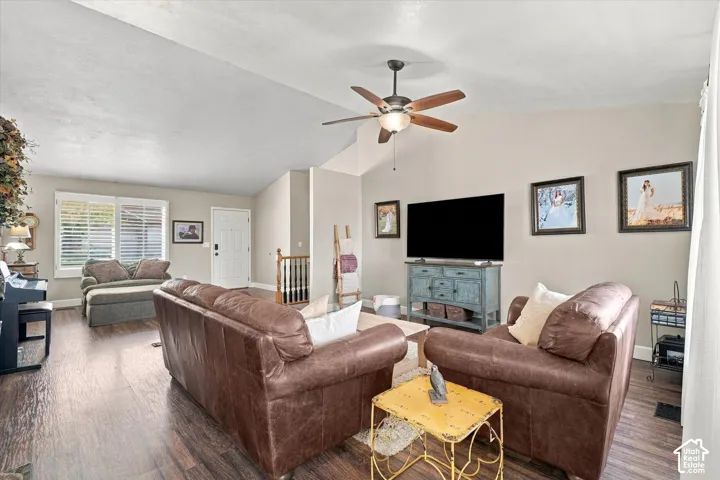 Living area featuring vaulted ceilings, wood-finish flooring, plantation shutters, and a ceiling fan with integrated lighting