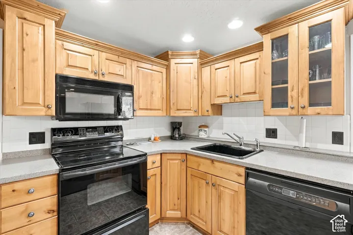 Kitchen featuring natural wood-finish cabinetry, solid-surface countertops, a tiled backsplash, glass-front upper cabinet doors, and integrated black appliances
