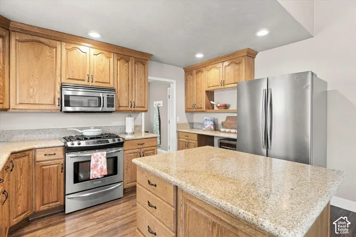 Kitchen featuring light-tone wood cabinetry, stone countertops, stainless steel appliances, a central island, and wood-finish flooring