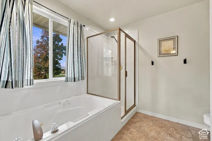 Soaking tub with integrated faucet, glass-enclosed shower with metal framing, recessed lighting, and tile flooring