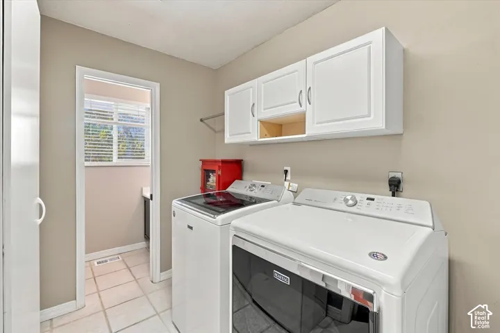 Laundry space featuring white shaker-style wall cabinetry, ceramic tile flooring, and a window with blinds