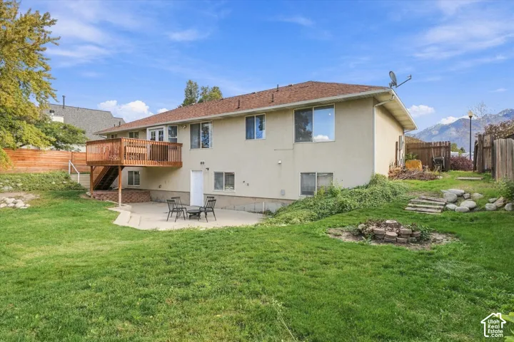 Stucco exterior featuring an elevated wood deck, concrete patio, stone-lined fire pit area, and wood-paneled privacy fencing