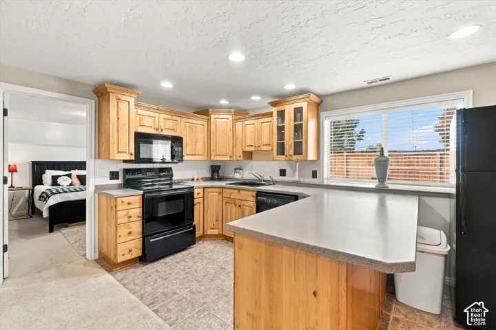 Kitchen featuring natural wood cabinetry, solid-surface countertops, tile flooring, and integrated black appliances