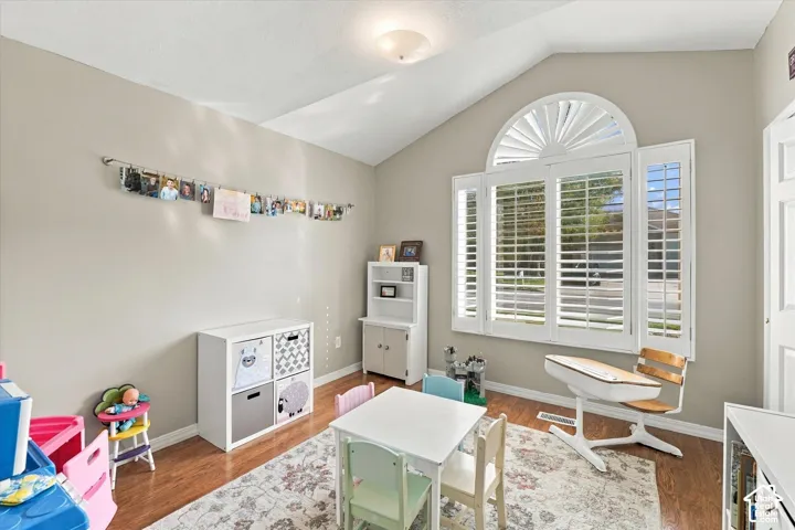Vaulted ceiling, wood-finish flooring, and arched window featuring plantation shutters
