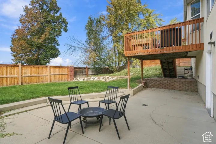 Rear exterior featuring a concrete patio, elevated wood deck with railing, tiered landscape wall, and wood privacy fencing