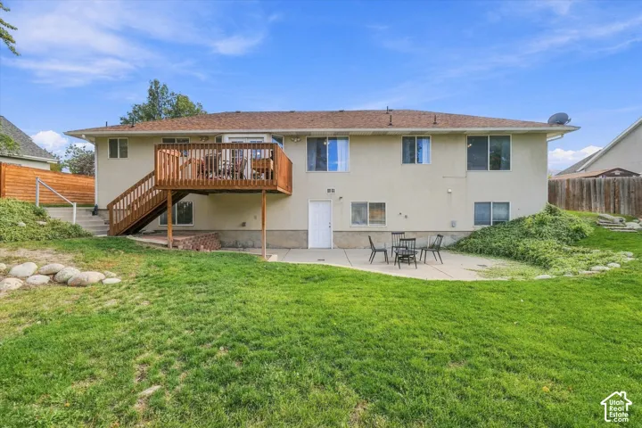 Rear exterior featuring a raised wooden deck with stairs, a concrete patio, and a fenced backyard