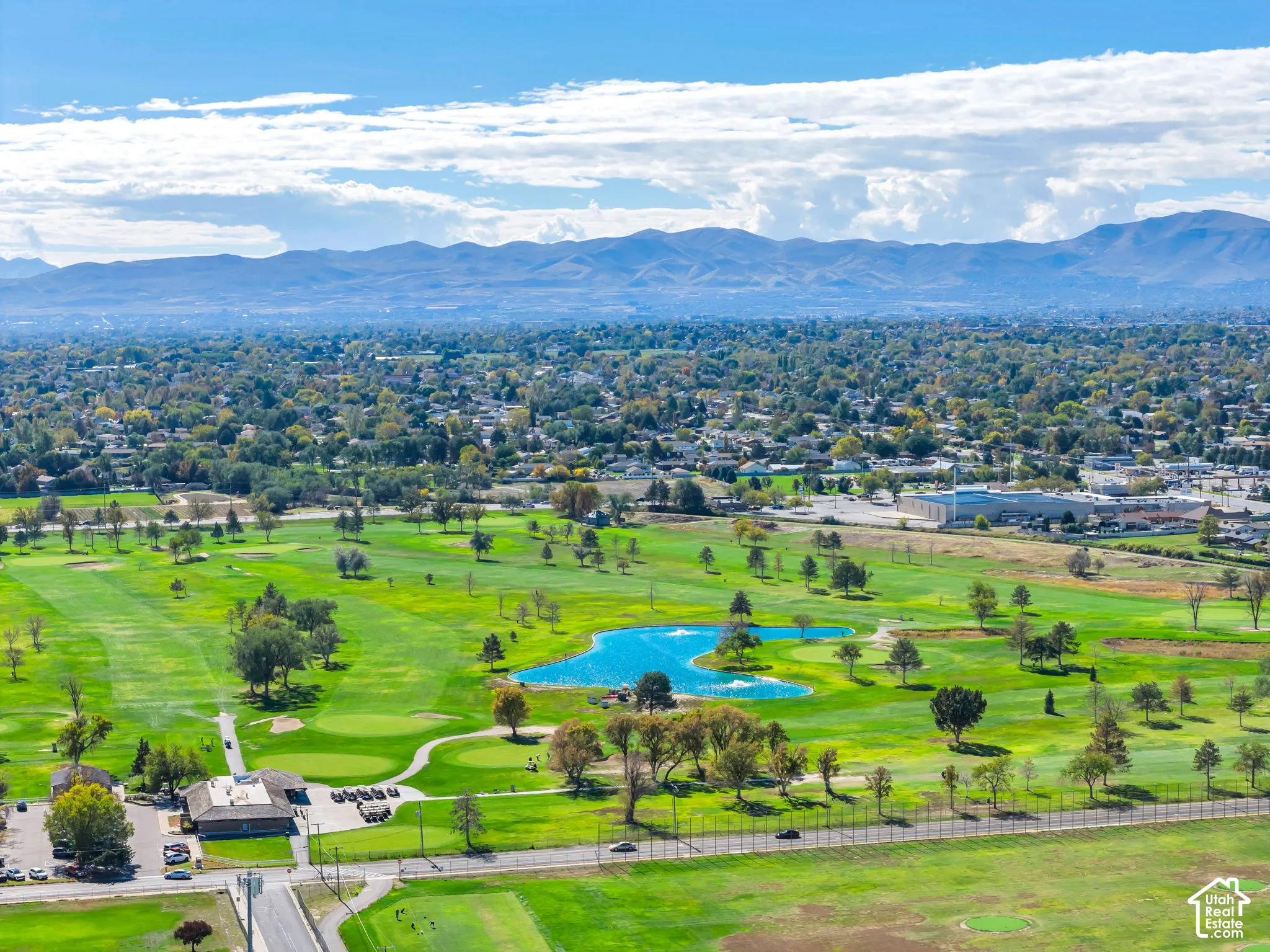 Aerial perspective featuring expansive golf course fairways, a central water feature, mature landscaping, and mountain backdrops