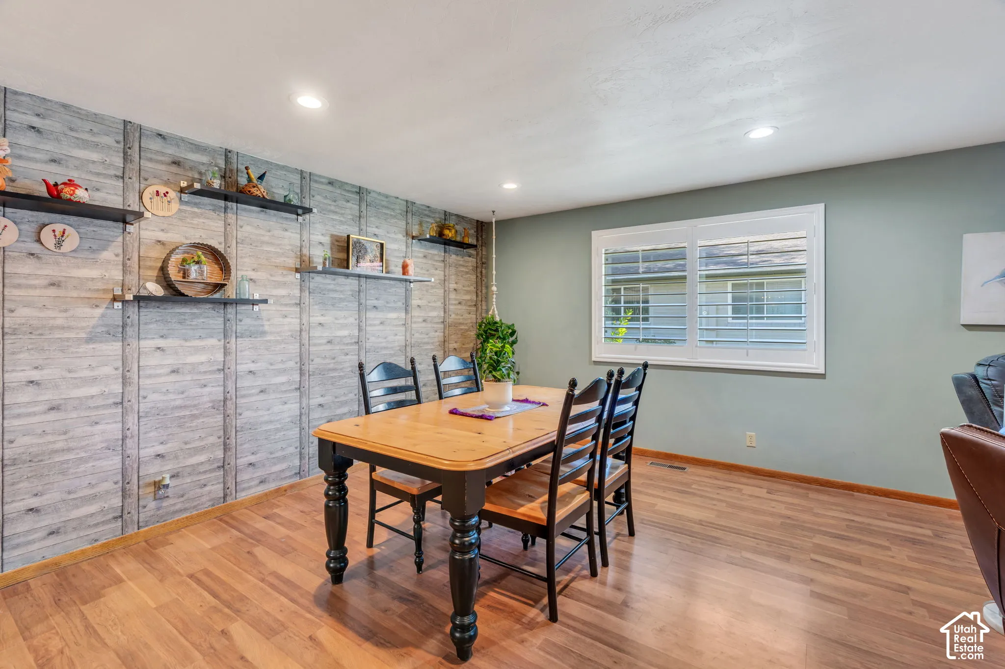Interior space featuring wood-finish flooring, recessed lighting, white shutter window treatments, and an accent wall with vertical trim detailing and mounted shelving