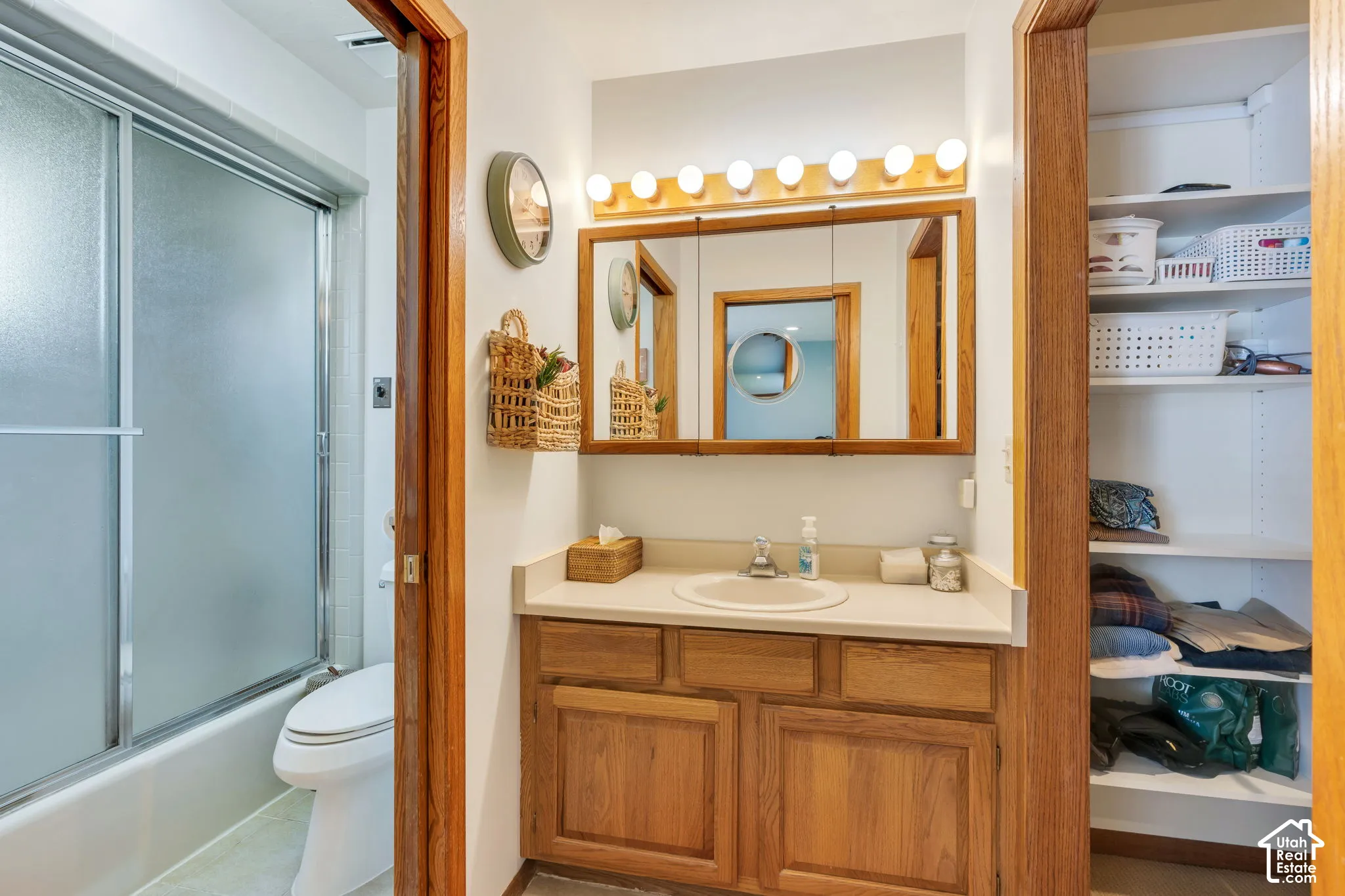 Bathroom featuring a wood vanity with a solid-surface countertop, an integrated sink, a tri-fold medicine cabinet, a Hollywood-style vanity light, and a tub-shower combination with sliding glass doors