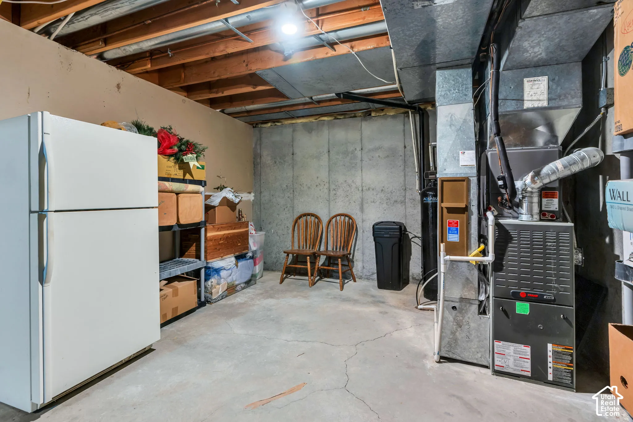 Utility area featuring a concrete floor, exposed wooden ceiling joists, poured concrete walls, and a dedicated furnace system