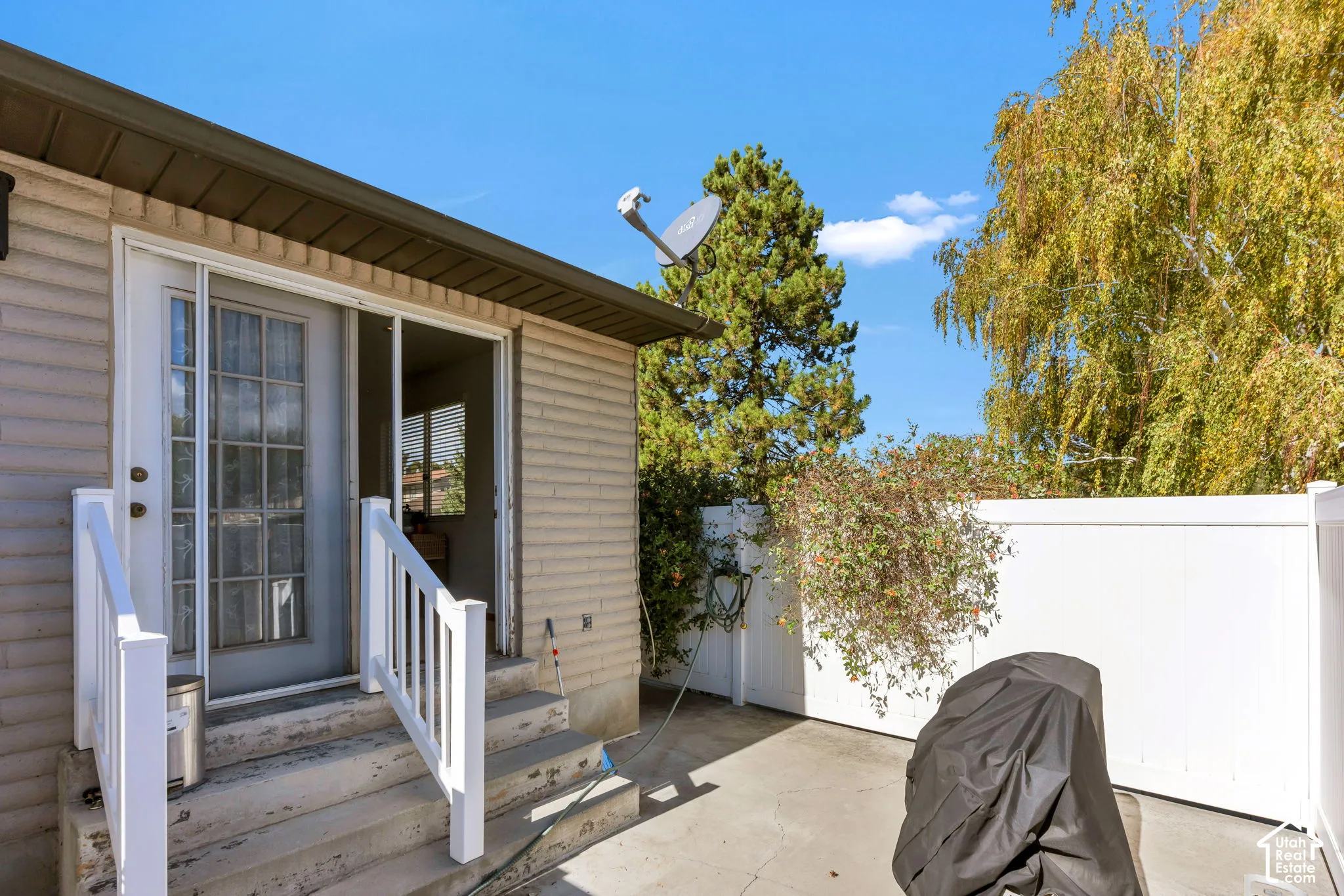 Exterior patio featuring a concrete surface, white vinyl privacy fencing, and concrete steps with white railing leading to a multi-lite glass door