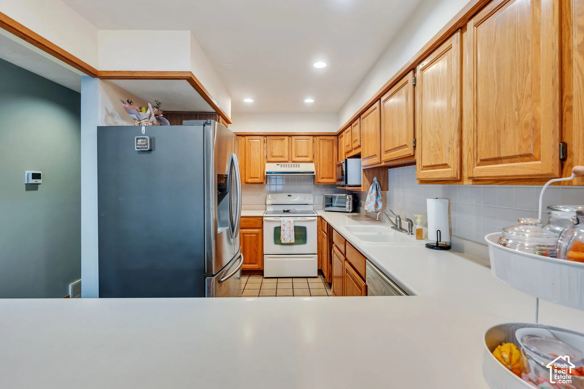 Kitchen featuring wood cabinetry, stainless steel refrigerator, solid-surface countertops, tile backsplash, and recessed lighting