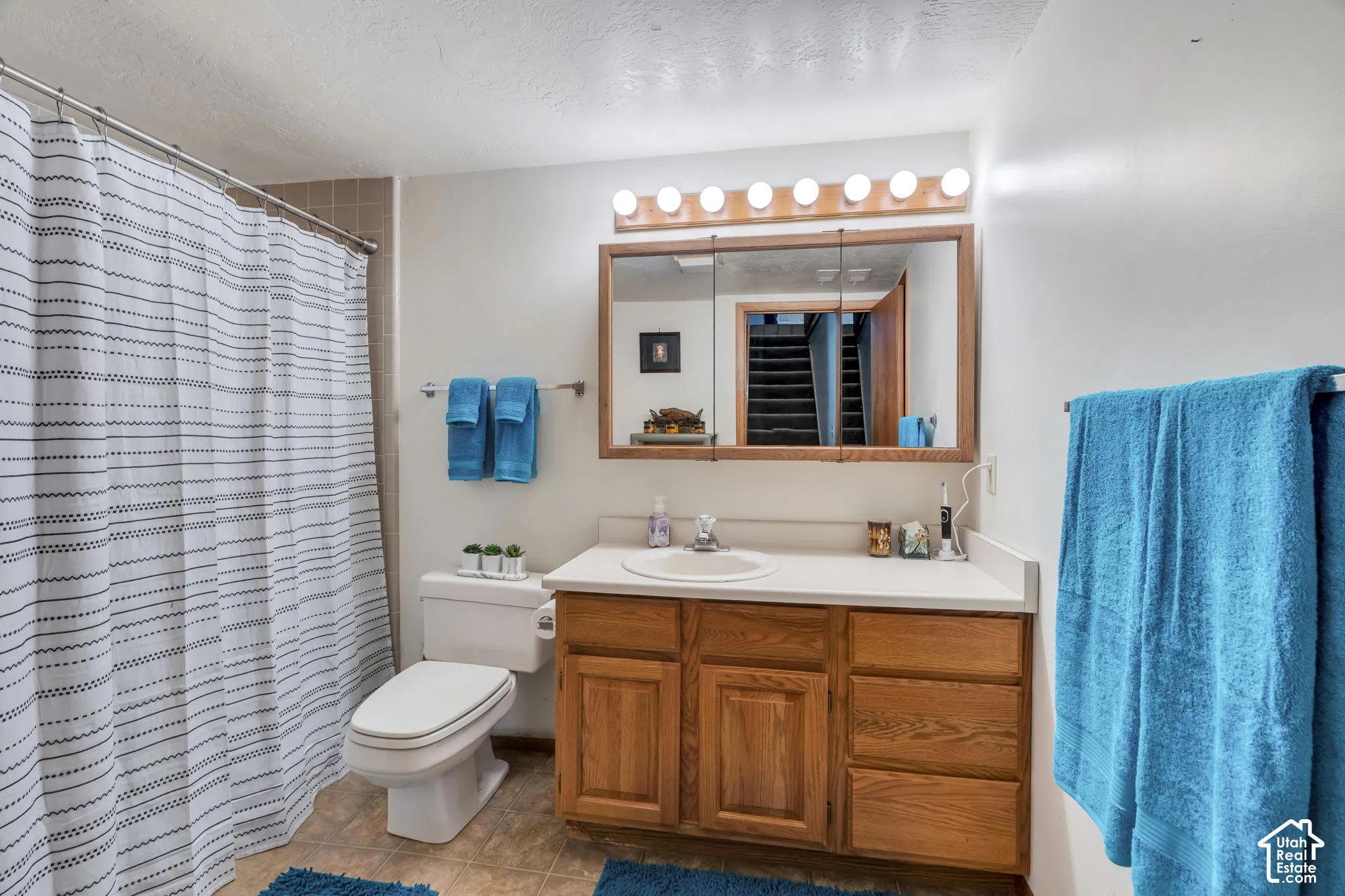 Bathroom featuring a wood-finish vanity with a white countertop, inset sink, large medicine cabinet with integrated lighting, and a shower-tub combination