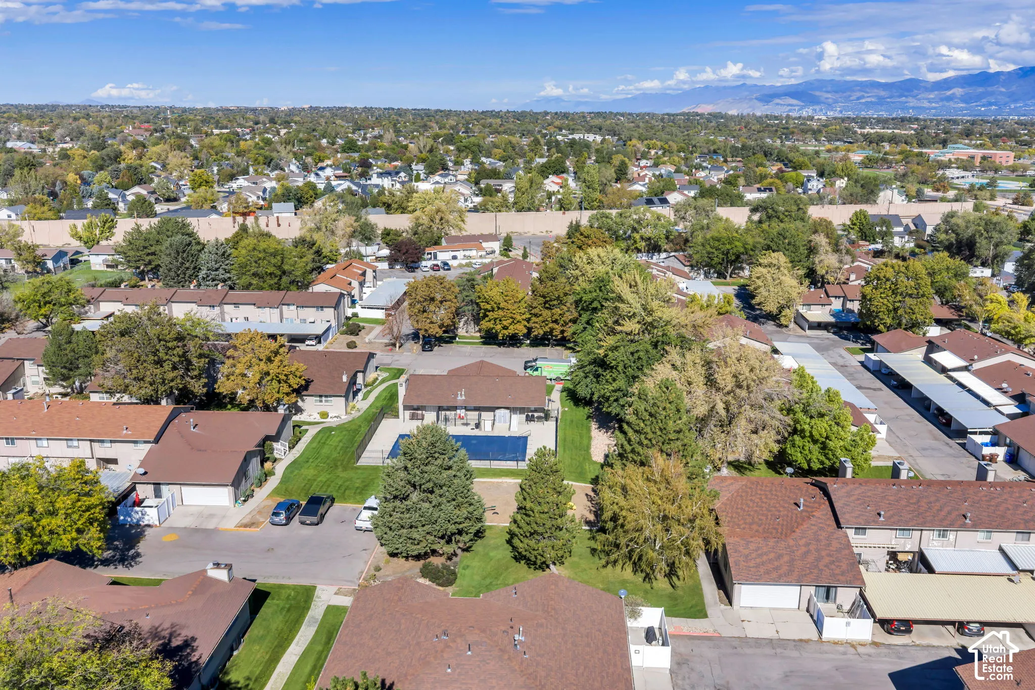 Aerial perspective of residential community featuring a swimming pool, expansive lawn areas, mature tree canopy, and mountain backdrop