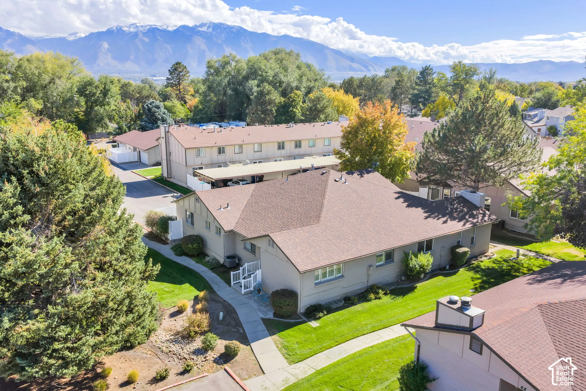 Aerial perspective of property featuring shingle roofing, mature trees, expansive manicured lawn, concrete walkways, and mountain backdrop