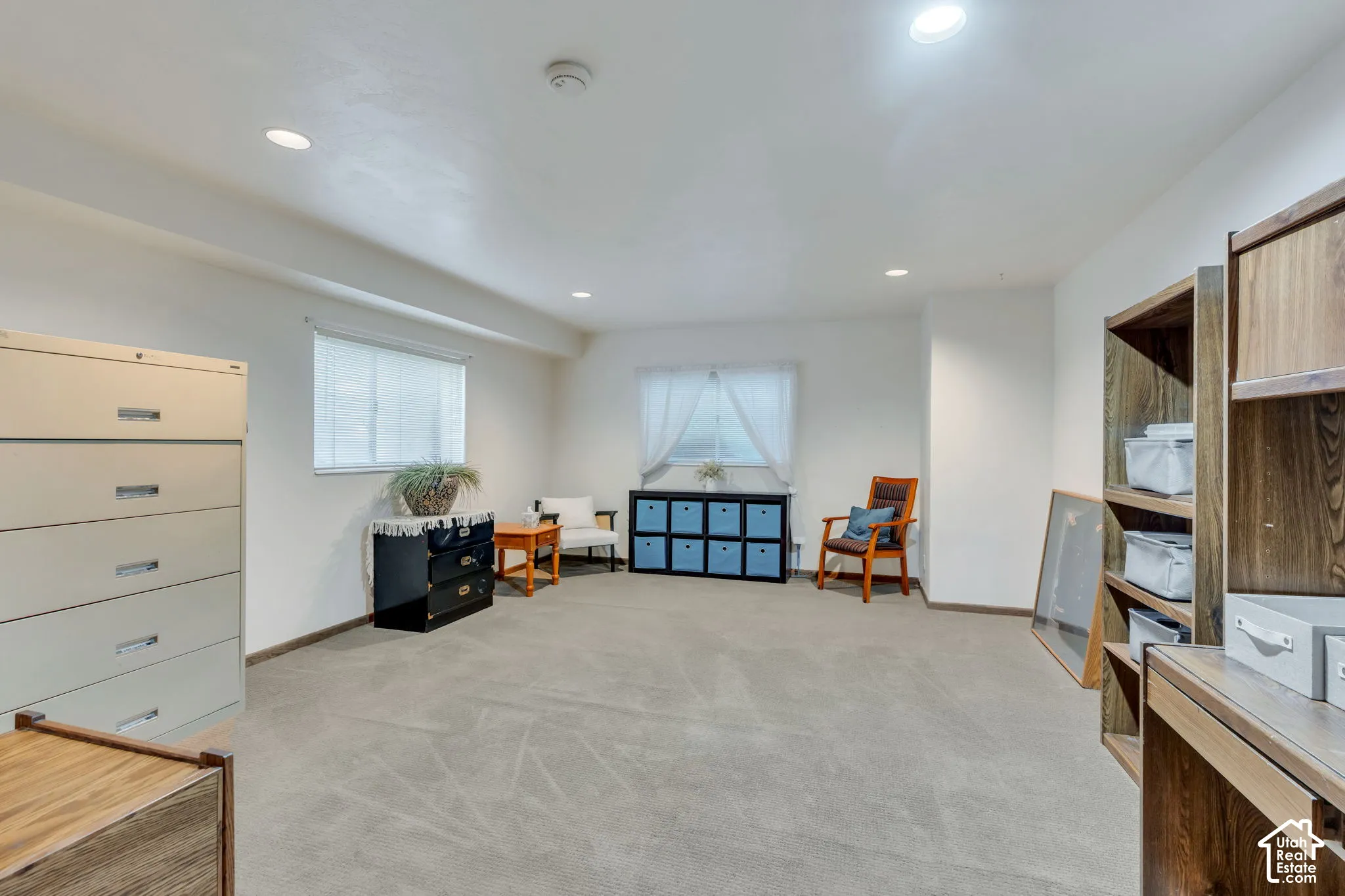 Spacious interior room featuring neutral carpeting, recessed ceiling lighting, and two windows providing natural illumination