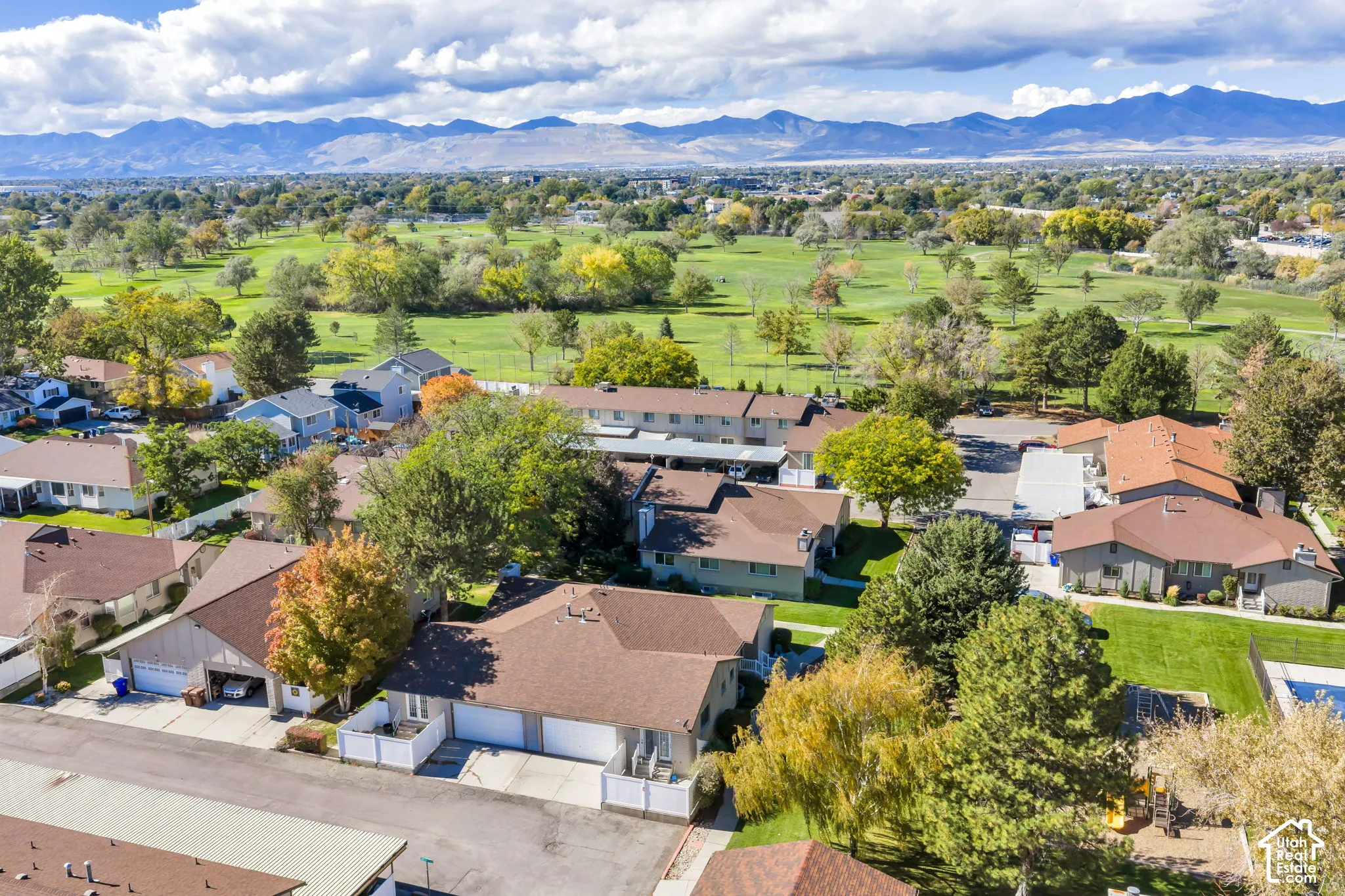 Aerial perspective featuring single-story residential dwellings with shingled roofing, attached garage parking, and mature landscaping, set against a backdrop of mountainous terrain