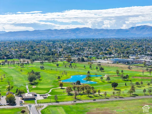 Aerial perspective featuring expansive golf course fairways, a central water feature, mature landscaping, and mountain backdrops