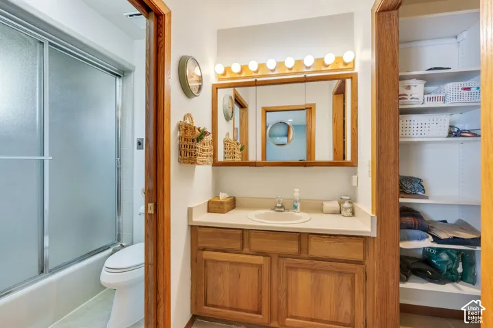 Bathroom featuring a wood vanity with a solid-surface countertop, an integrated sink, a tri-fold medicine cabinet, a Hollywood-style vanity light, and a tub-shower combination with sliding glass doors