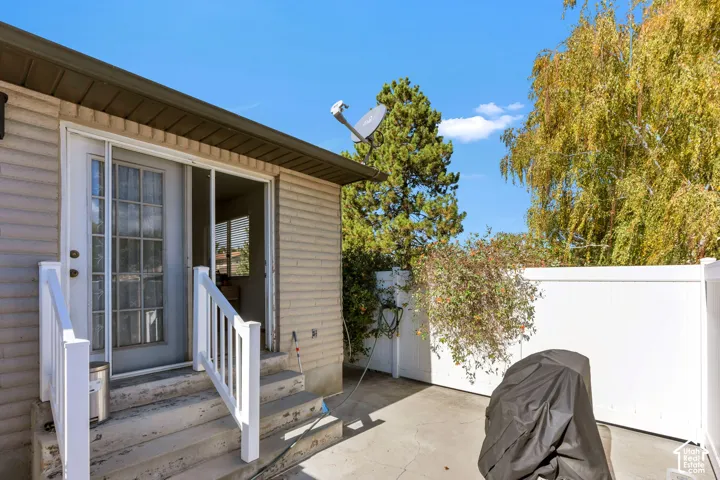 Exterior patio featuring a concrete surface, white vinyl privacy fencing, and concrete steps with white railing leading to a multi-lite glass door
