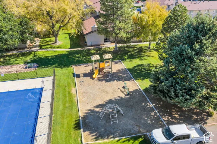 Outdoor recreation area featuring a playground with climbing structures and slides, fenced swimming pool, and landscaped grounds with mature trees