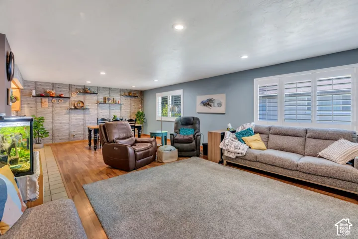 Living area featuring wood-finish flooring, recessed lighting, plantation shutters, and a decorative paneled accent wall with built-in shelving