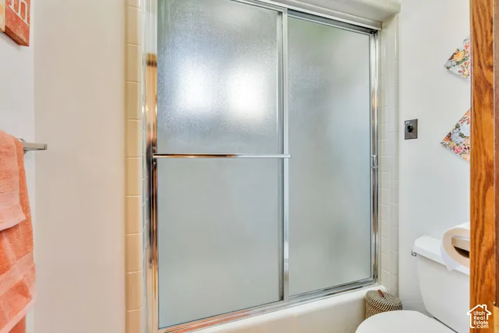 Shower enclosure featuring sliding semi-opaque glass doors, chrome frame, and neutral tile surround