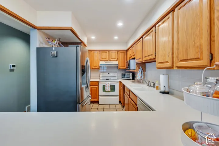 Kitchen featuring wood cabinetry, stainless steel refrigerator, solid-surface countertops, tile backsplash, and recessed lighting