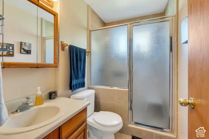 Bathroom featuring a wood-finish vanity cabinet, integrated sink with chrome faucet, medicine cabinet with mirrored doors, and a shower enclosure with frosted glass panels and tile surround