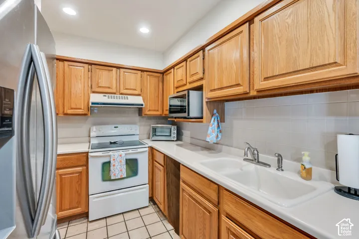 Kitchen featuring natural wood cabinetry, white tile backsplash, solid-surface countertops, dual-basin white sink, and recessed lighting
