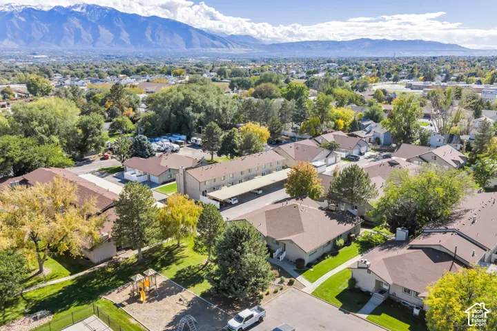 Aerial perspective featuring mountain backdrops, mature trees, manicured lawns, a dedicated play area, and covered parking structures