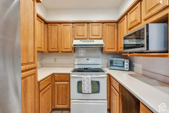 Kitchen featuring shaker-style wood cabinetry, white tile backsplash, solid-surface countertops, and an integrated range hood