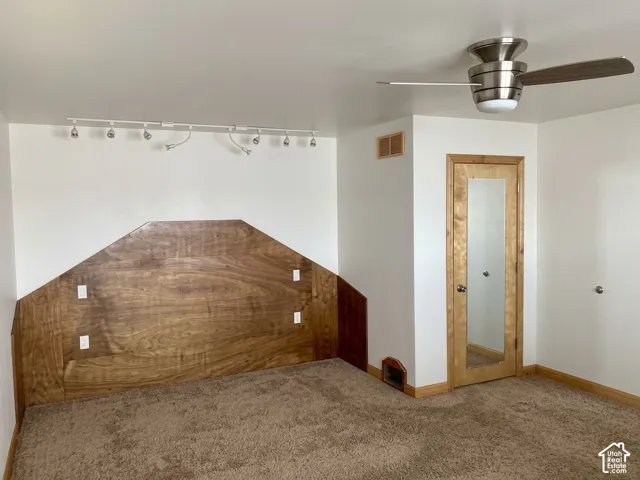 Room featuring a geometric wood-paneled accent wall, neutral carpeting, brushed nickel ceiling fan, track lighting, and a door with an integrated mirror