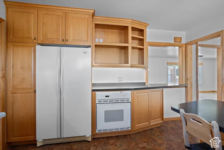 Kitchen featuring natural wood cabinetry, built-in open shelving, dark countertops, and integrated wall-mount oven