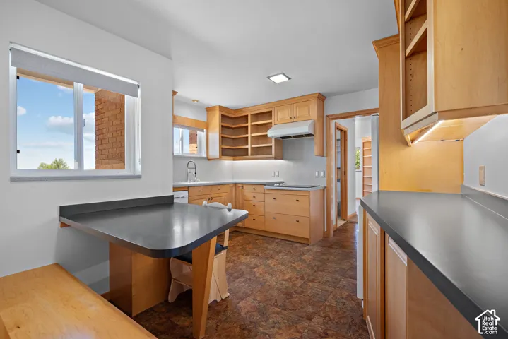 Kitchen featuring light wood cabinetry, dark solid-surface countertops, integrated breakfast bar, recessed lighting, and resilient flooring