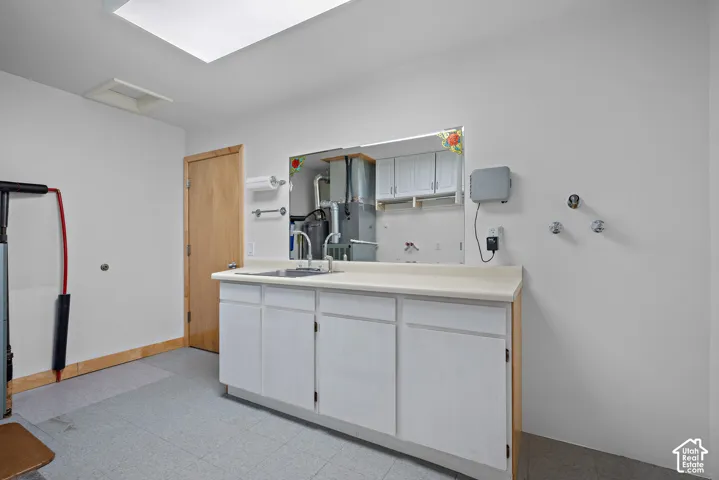 Utility space featuring white base cabinetry, integrated sink with faucet, large wall-mounted mirror, and tile flooring
