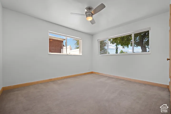 Neutral-toned interior room featuring wall-to-wall carpeting, two horizontal sliding windows, and a brushed nickel ceiling fan with integrated lighting