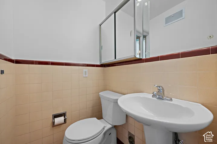 Pedestal sink with polished chrome faucet, mirrored medicine cabinet, and square ceramic wall tiling featuring a decorative accent border