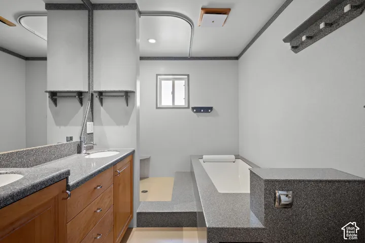 Dual-sink vanity with stone-finish countertop, step-up soaking tub, integrated stone-finish tub surround, and walk-in shower area