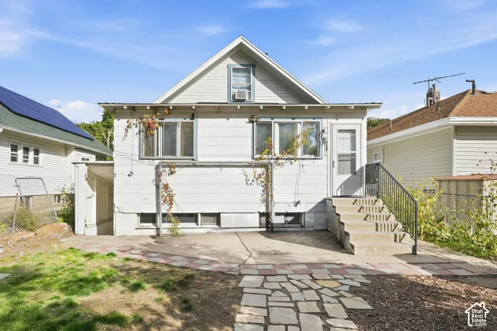Exterior rear elevation featuring horizontal siding, a gabled roofline, concrete patio, stone-tiled walkway, and concrete stairs with metal handrails