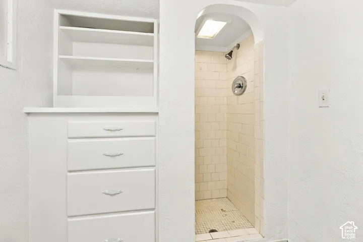 Built-in white storage cabinetry featuring open shelving and four drawers, complemented by an arched shower alcove with tile surround and integrated lighting