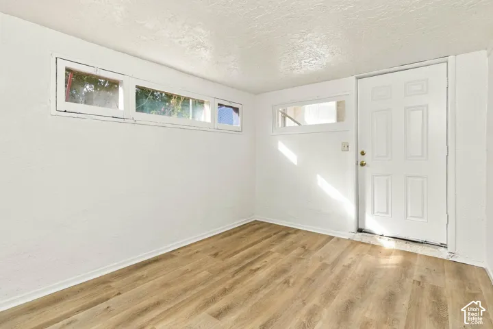 Wood-finish flooring, textured white wall finish, multi-pane casement windows, and a six-panel entry door