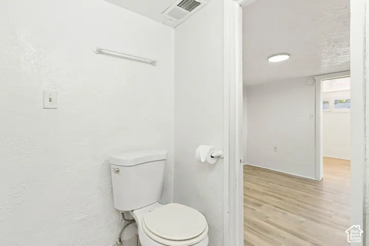 White toilet with wall-mounted towel bar, flush-mounted circular ceiling lighting, and wood-finish flooring